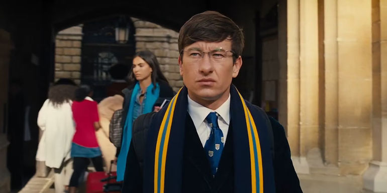 Oliver is wearing glasses and a suit while walking through campus in Saltburn.