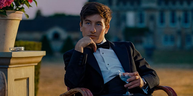 Oliver is sitting and holding a drink with the estate behind him in Saltburn.