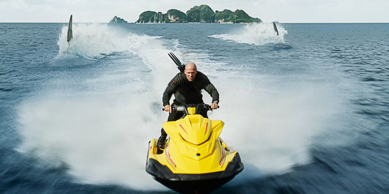 Jason Statham as Jonas Taylor riding away from two megs on a jet ski in Meg 2 The Trench