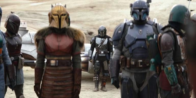 Din Djarin leans against his N-1 starfighter behind the Armorer and Paz Vizsla in The Mandalorian season 3 episode 5