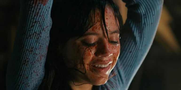 Jenna Ortega's Tara smiles while crying and covered in blood with arms raised in Scream 6