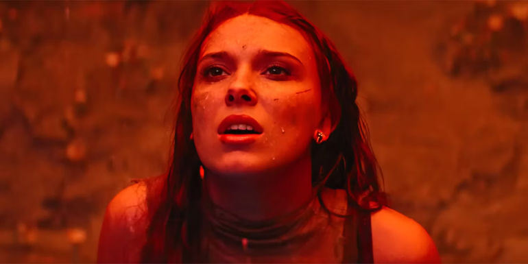 Millie Bobby Brown in a red light looking up in Damsel trailer