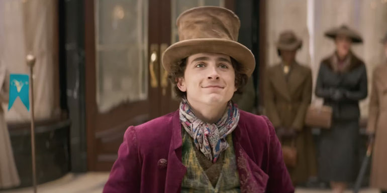 Timothee Chalamet as Willy Wonka standing in front of a colorful machine in Wonka