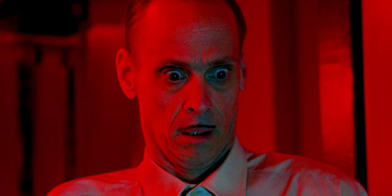 John Waters as Pete Peters Staring in Shock While Drenched in Red Light in Seed of Chucky