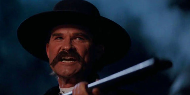 Kurt Russell As Wyatt Earp holding a shotgun and yelling In Tombstone