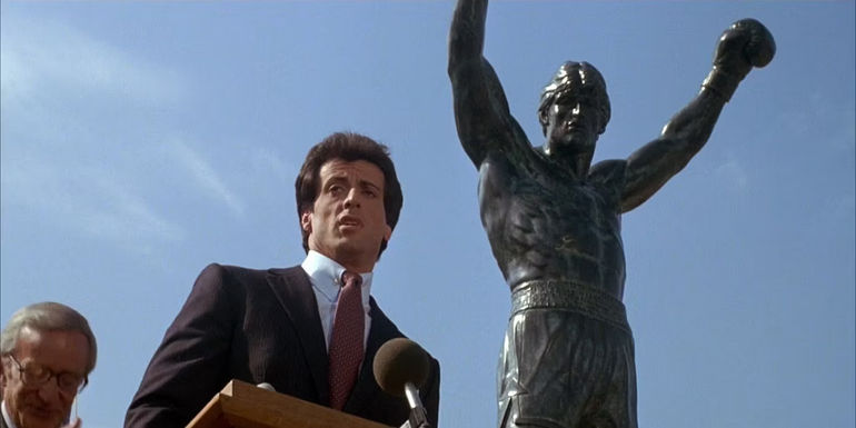 Sylvester Stallone at a podium in front of the Rocky statue in Rocky 3