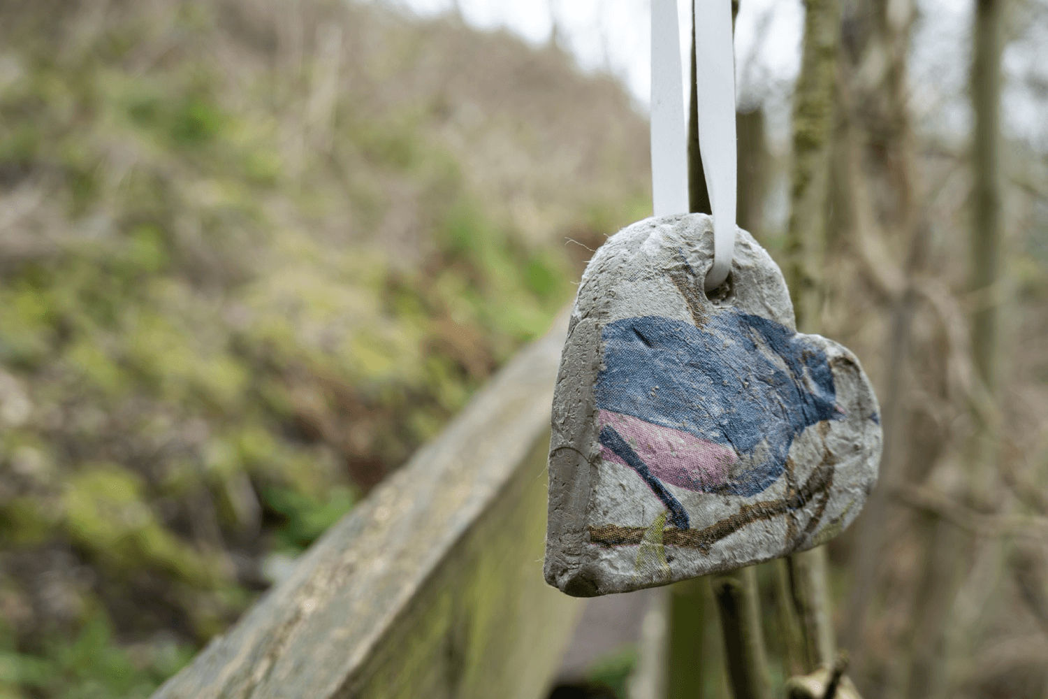 A painted heart pendant made of stone hanging from the branch of a tree