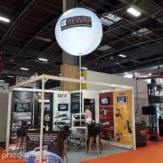 ballon publicitaire gonflé à l'air au dessus d'un stand sur un salon. moins cher que les ballons à l'hélium et plus facile à installer. option lumineuse pour une meilleure visibilité sur le salon.