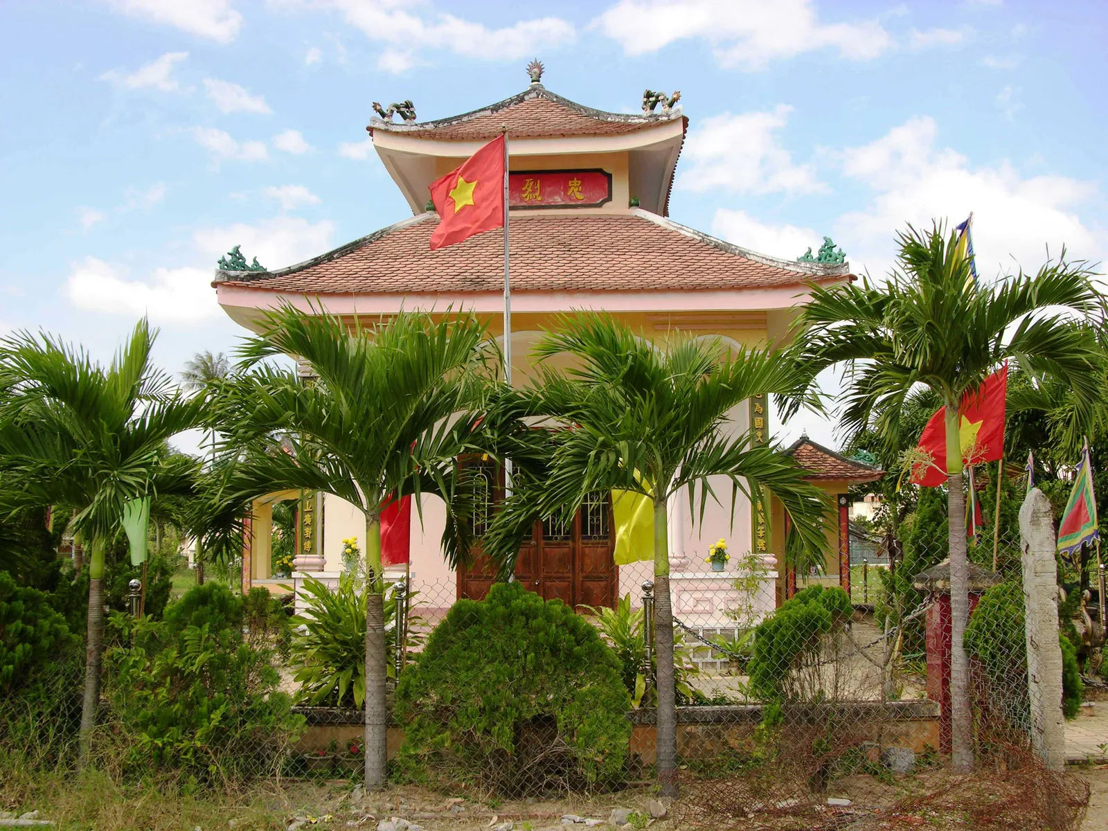 Đền thờ Trần Quý Cáp ở Diên Khánh nhìn từ ngoài hàng rào, cờ và hàng cau trước sân