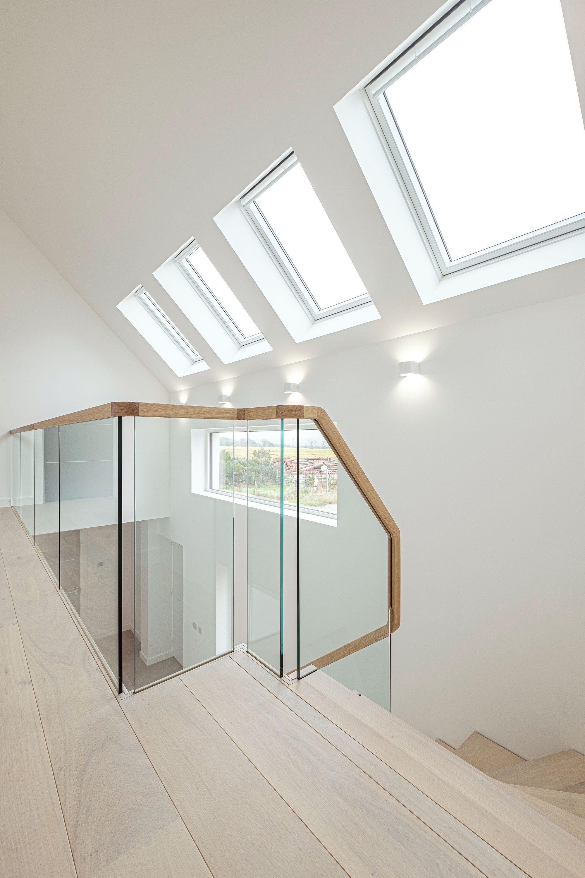 Top level view of glass balustrade in large, minimal, white house with four large windows.