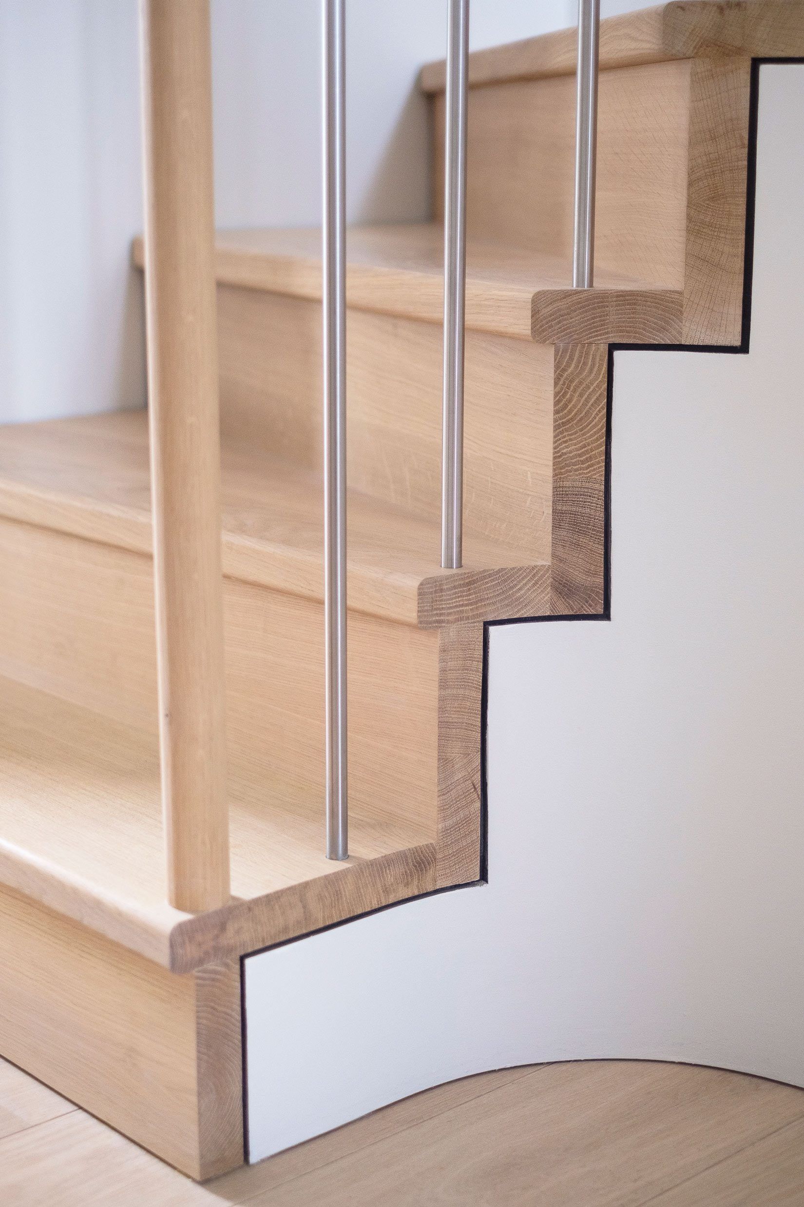 Detailed view of bottom of a staircase. Oak treads and risers, with white stringer and stainless steel spindles.