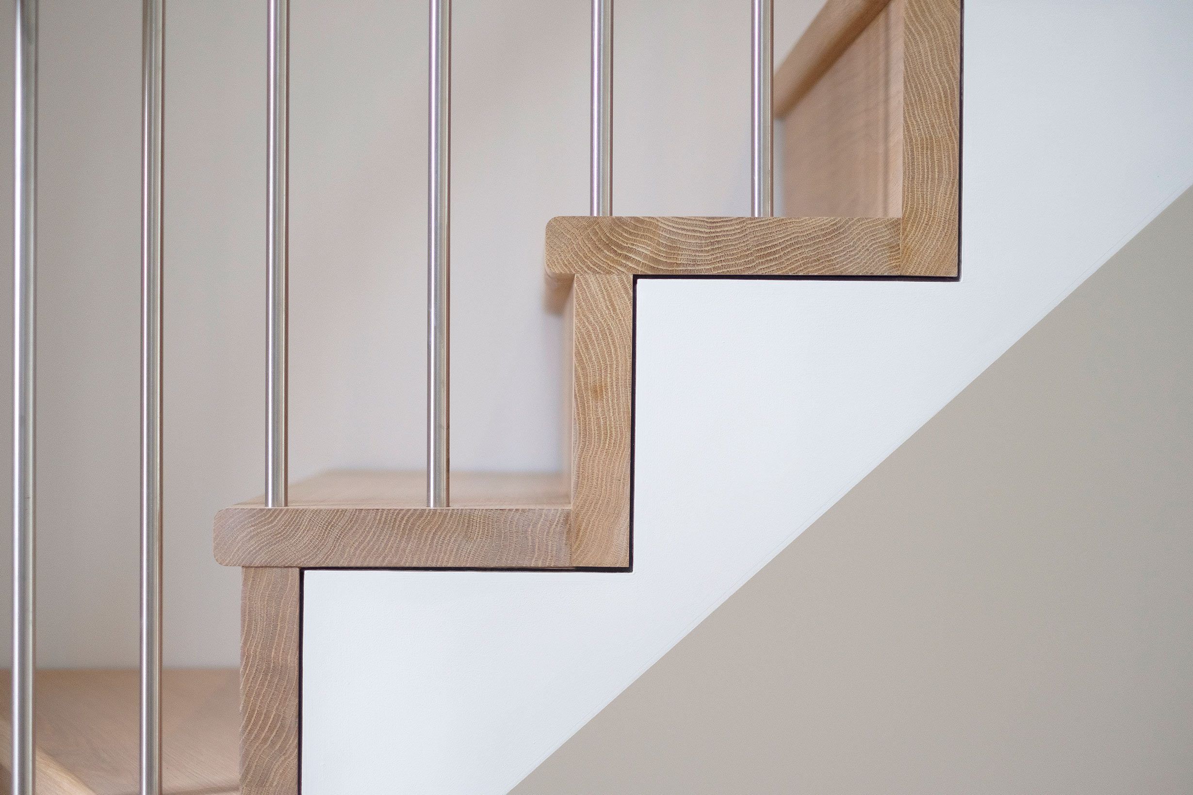 Side view detail of oak treads and risers, with white stringer and stainless steel spindles.