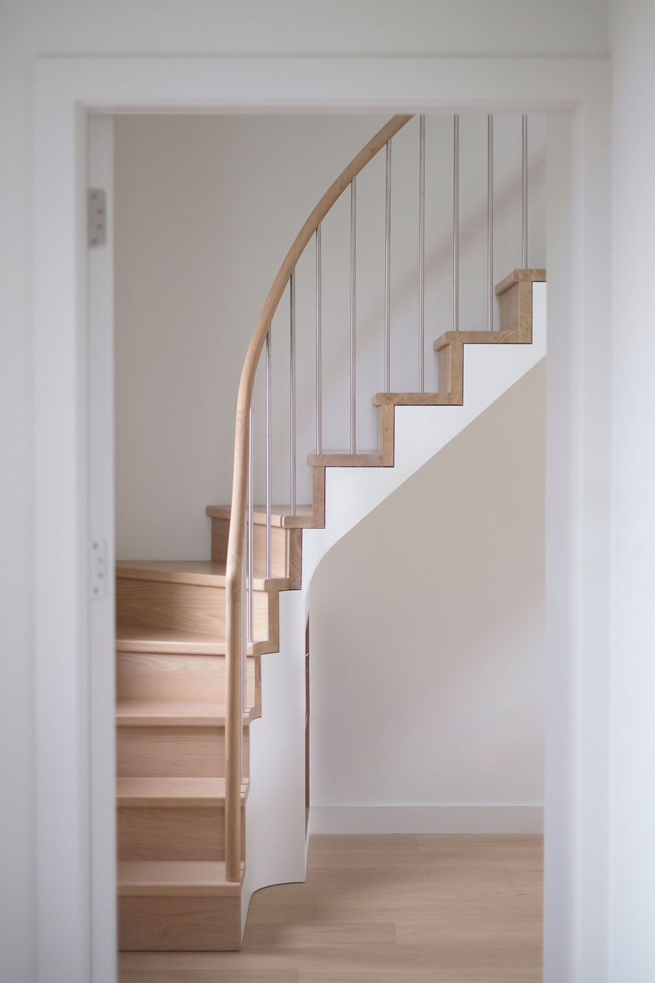 Oak staircase framed by open white door with curved handrail and stainless steel balustrade spindles.