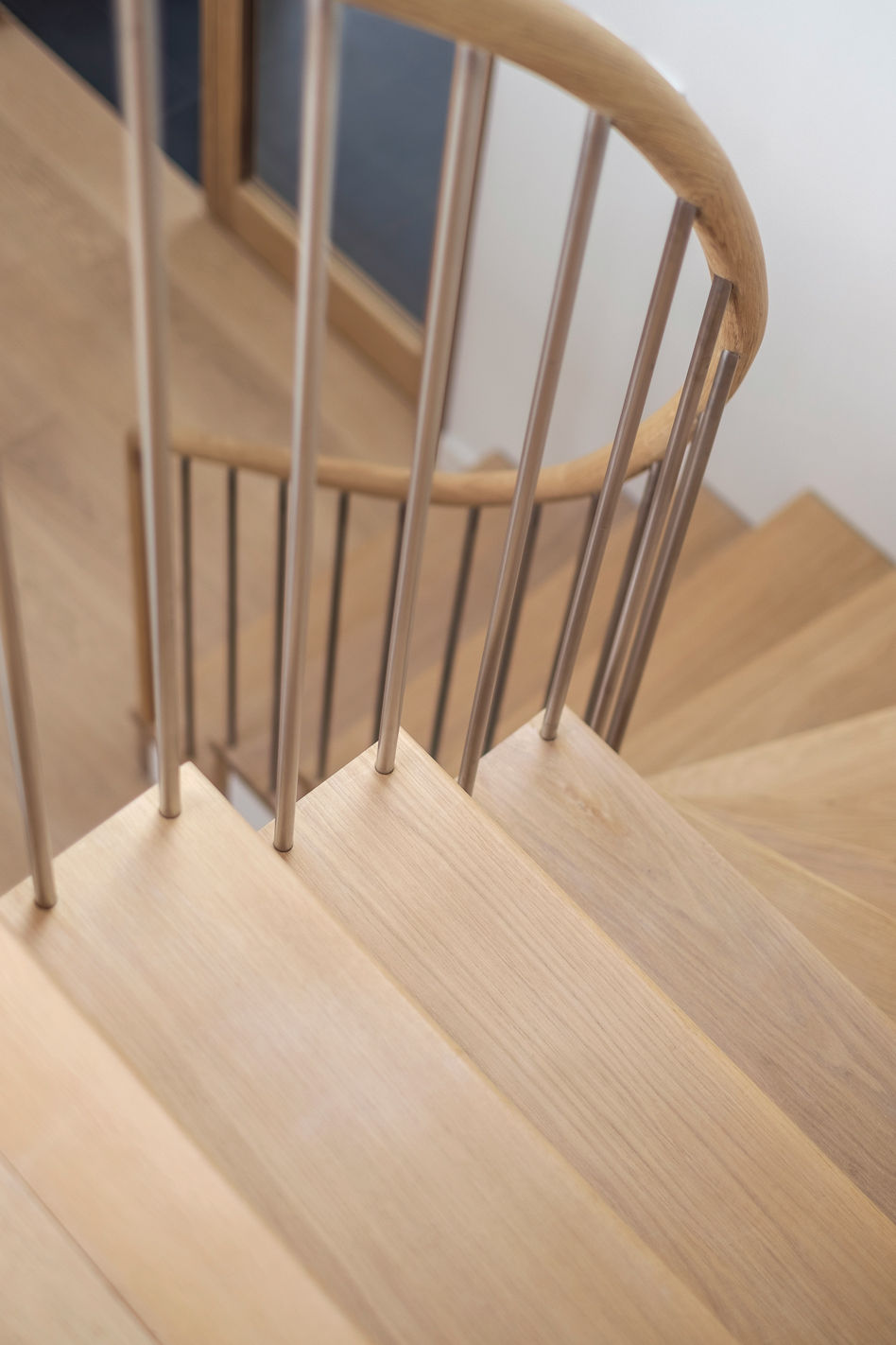 Downwards angle of oak staircase and curved oak handrail, with stainless steel spindles.