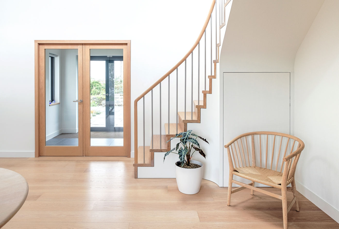 Oak domestic interior with Danish designed oak table and chair, oak staircase and handrail with stainless steel balustrade. Glazed oak Doors. White walls and potted plant.