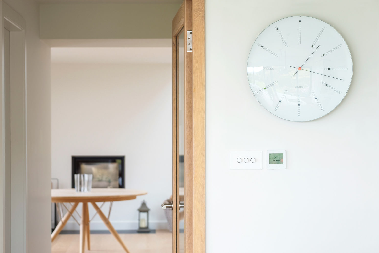 Classic domestic interior through a glazed oak door with Danish designed oak table and white clock on wall.