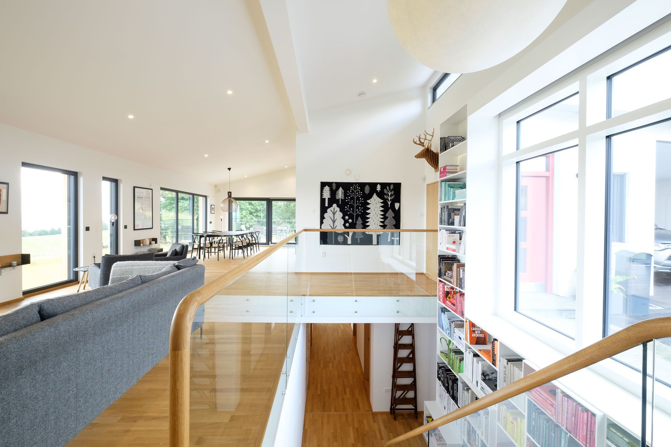 Sculptural Oak zig zag staircase with glass balustrade. White fitted bookcases with rows of books organised by colour.