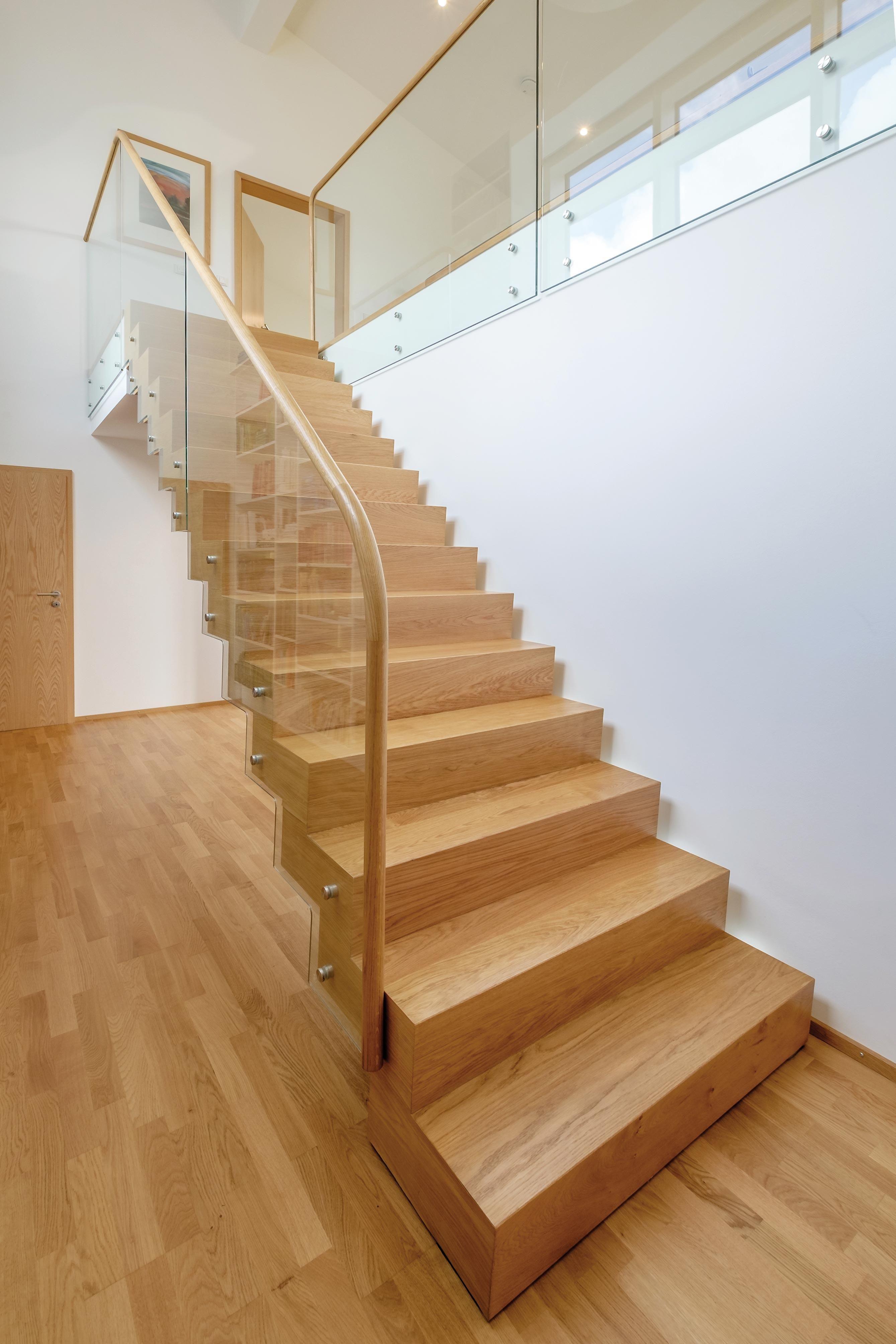 Side view of sculptural oak zig zag staircase with glass balustrade against white wall.