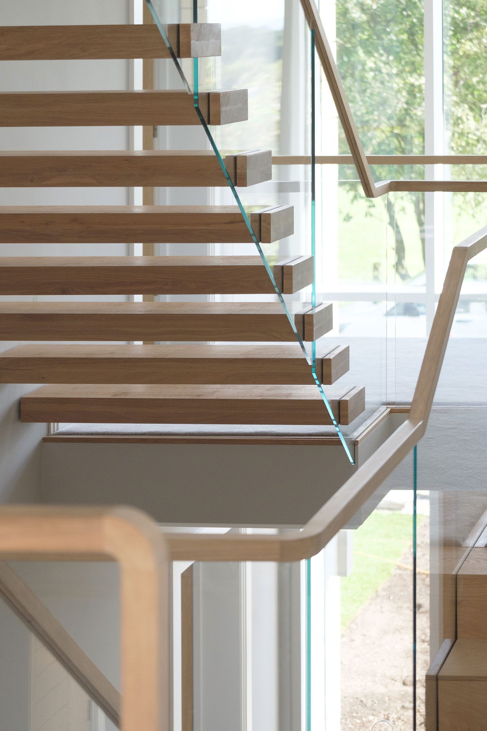 Underside of floating cantilevered oak staircase with glass balustrade. Grey walls and carpet with wood doors.