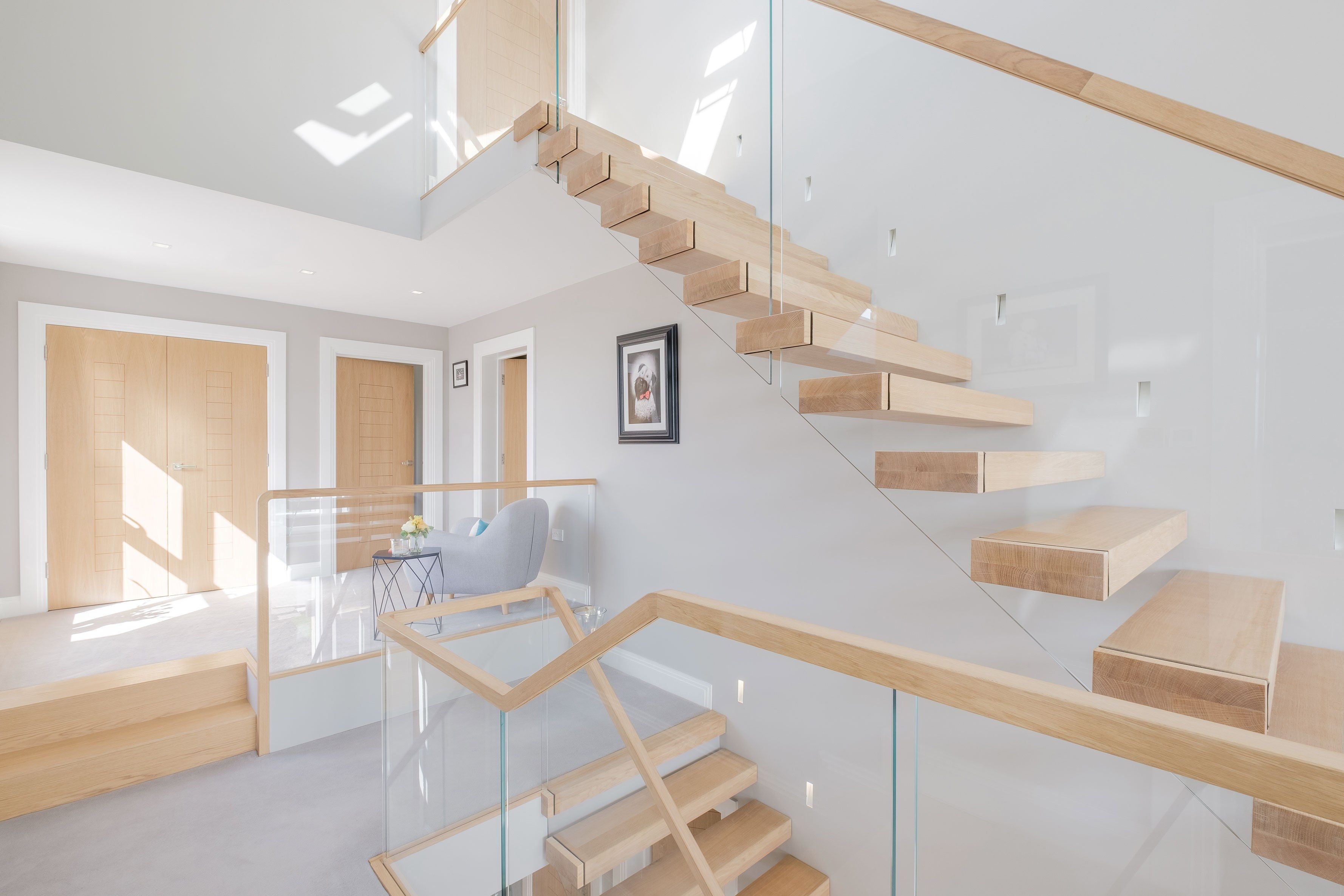 Side view of floating cantilevered oak stair with glass balustrade. Grey walls and carpet with wood doors.