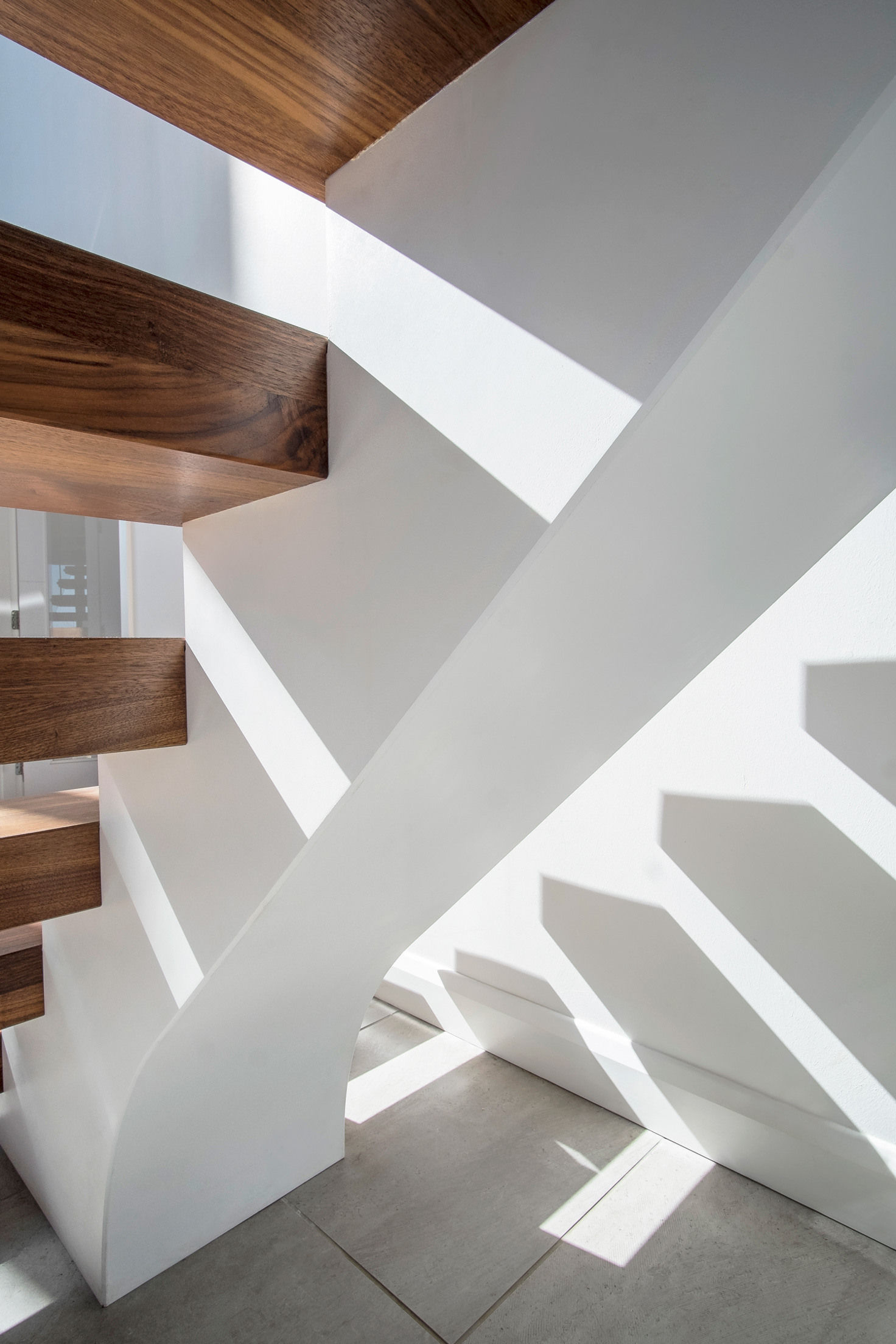 Underside of floating central stringer feature staircase with walnut treads, handrail and glass balustrade. Sunlight shining through spaces in staircase.