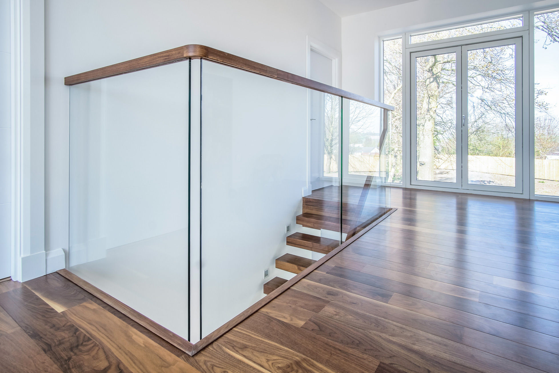 Contemporary glass balustrade of walnut staircase with walnut handrail.