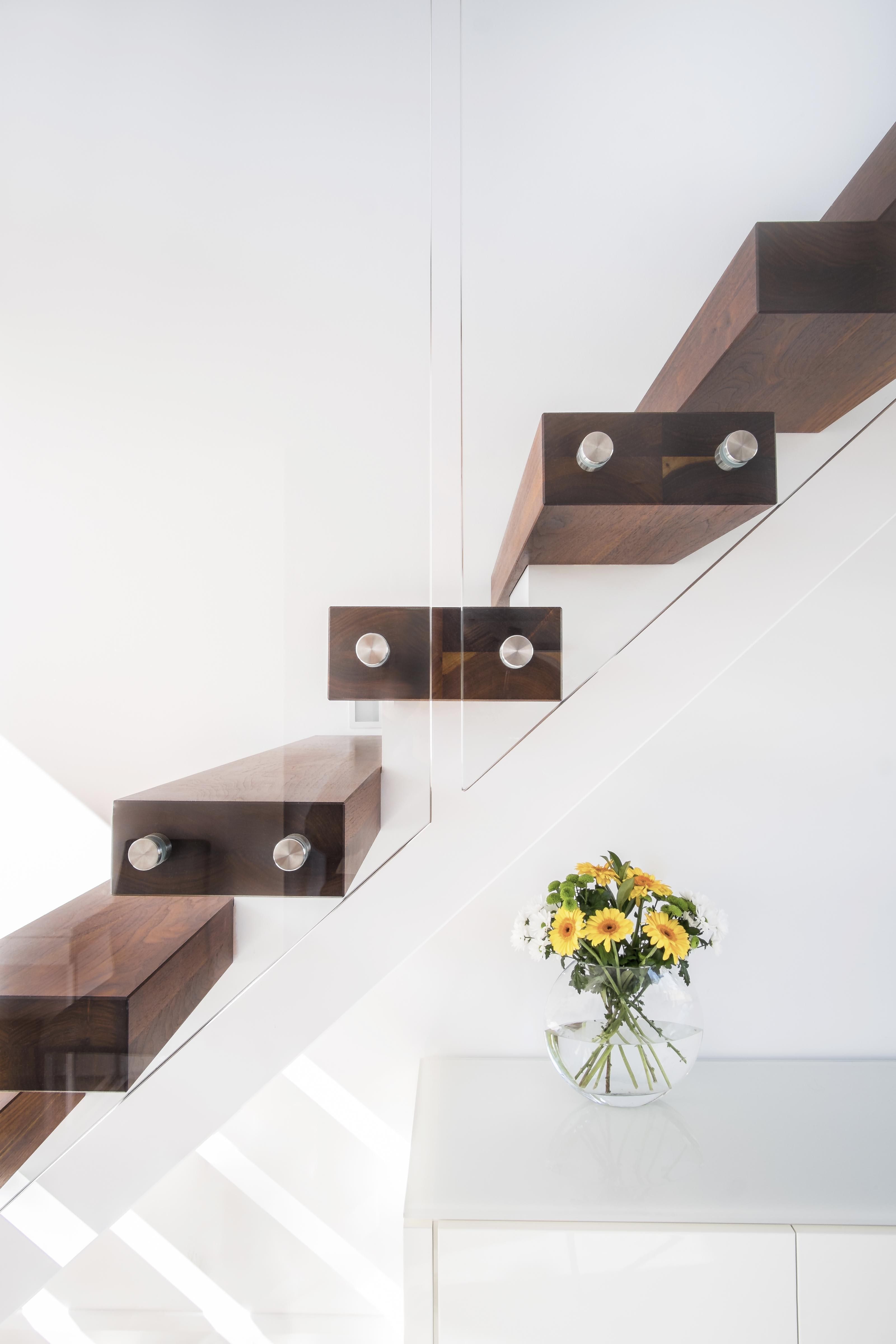 Side view of floating central stringer feature staircase with walnut treads, handrail and glass balustrade. White walls and white sideboard.