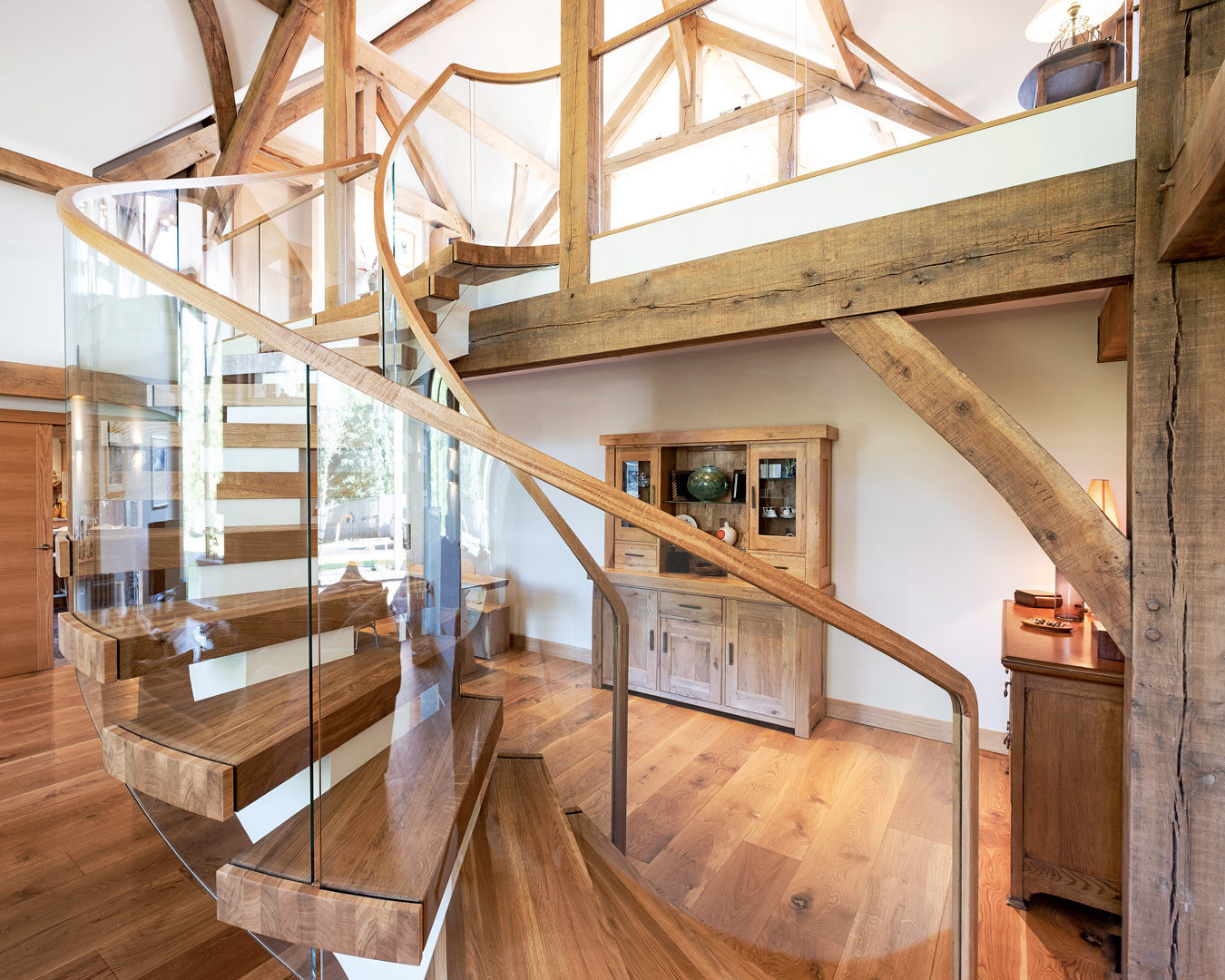 Curved floating oak stair centrepiece with curved glass in green oak framed modern home.