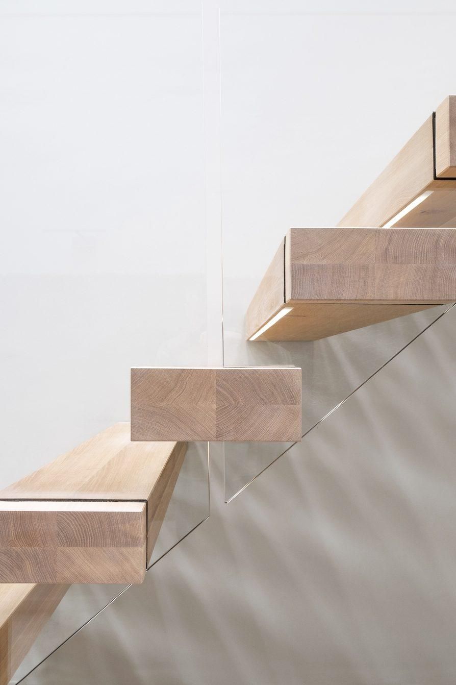 Side view of cantilevered feature staircase with oak treads and glass balustrade against white wall.