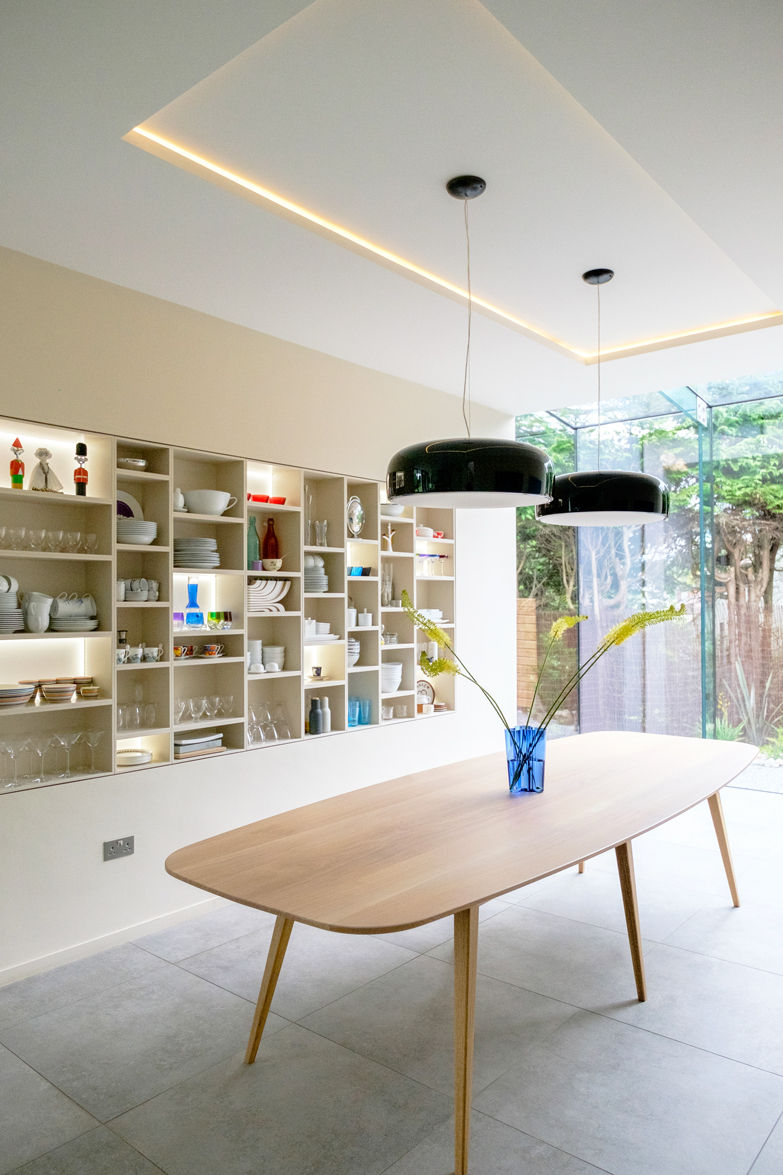 Bespoke fitted furniture filled with glassware and ceramics. Large wooden dining table and black light fixture. Blue vase with large yellow flowers on table.