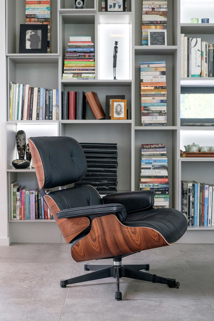 Eames lounge chair in front of fitted furniture filled with books, photographs and ornaments.