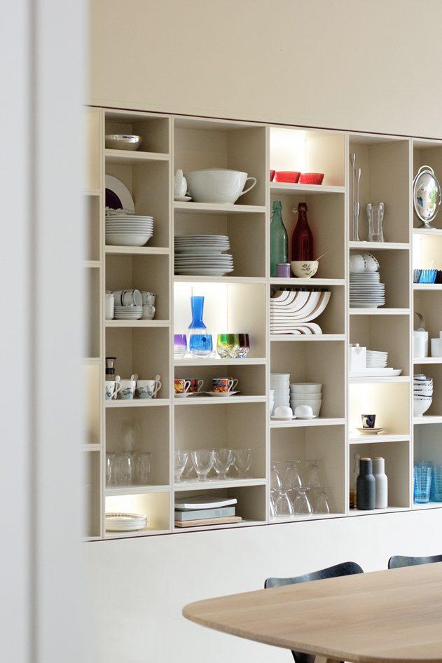 Bespoke display and storage shelving filled with glassware and ceramics. Wooden table and black light fixture.