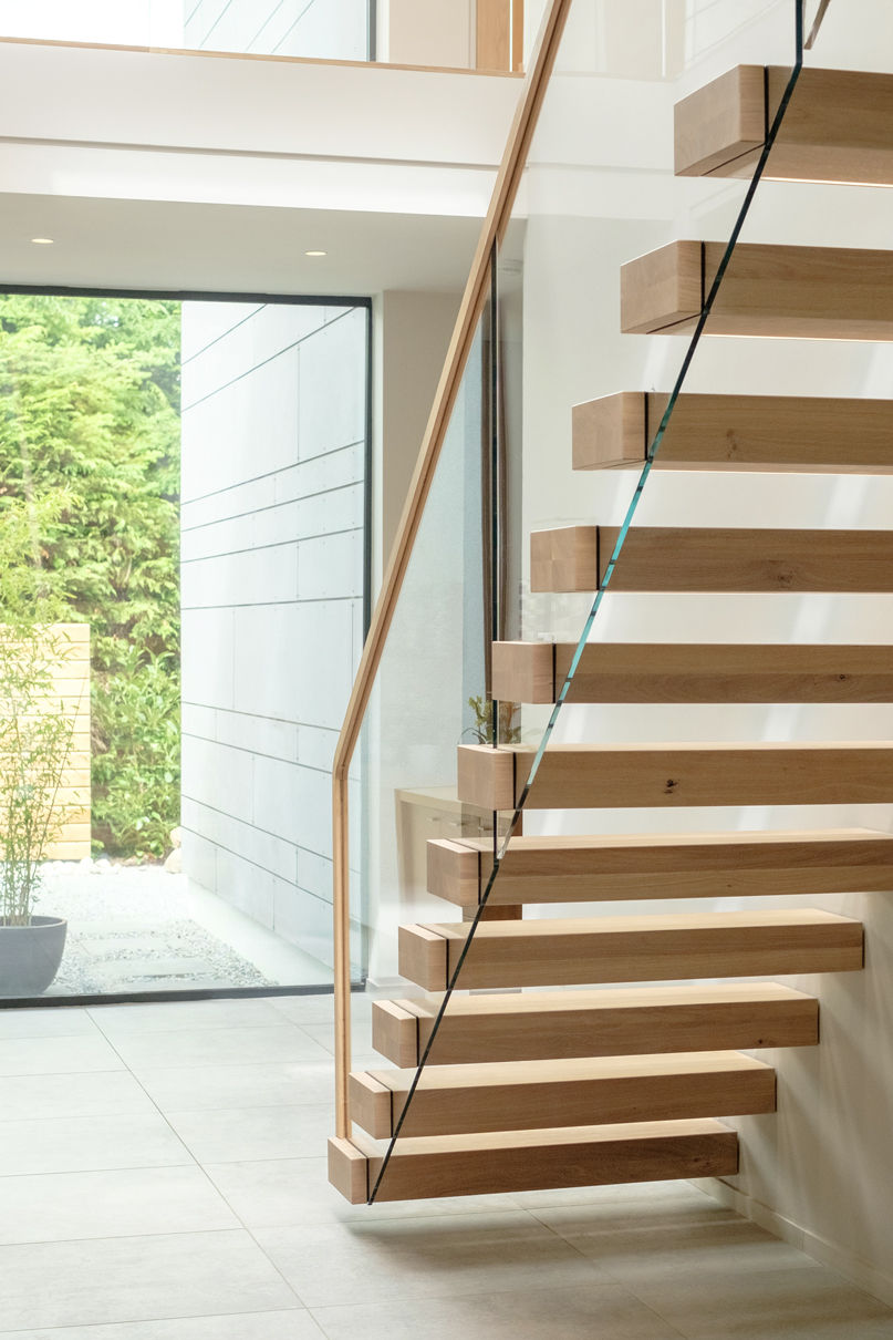 Underside of cantilevered feature staircase with oak treads and glass balustrade. Garden visible from window.