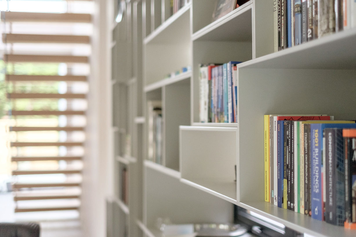 Side view of fitted furniture filled with books. Cantilevered staircase out of focus in background.