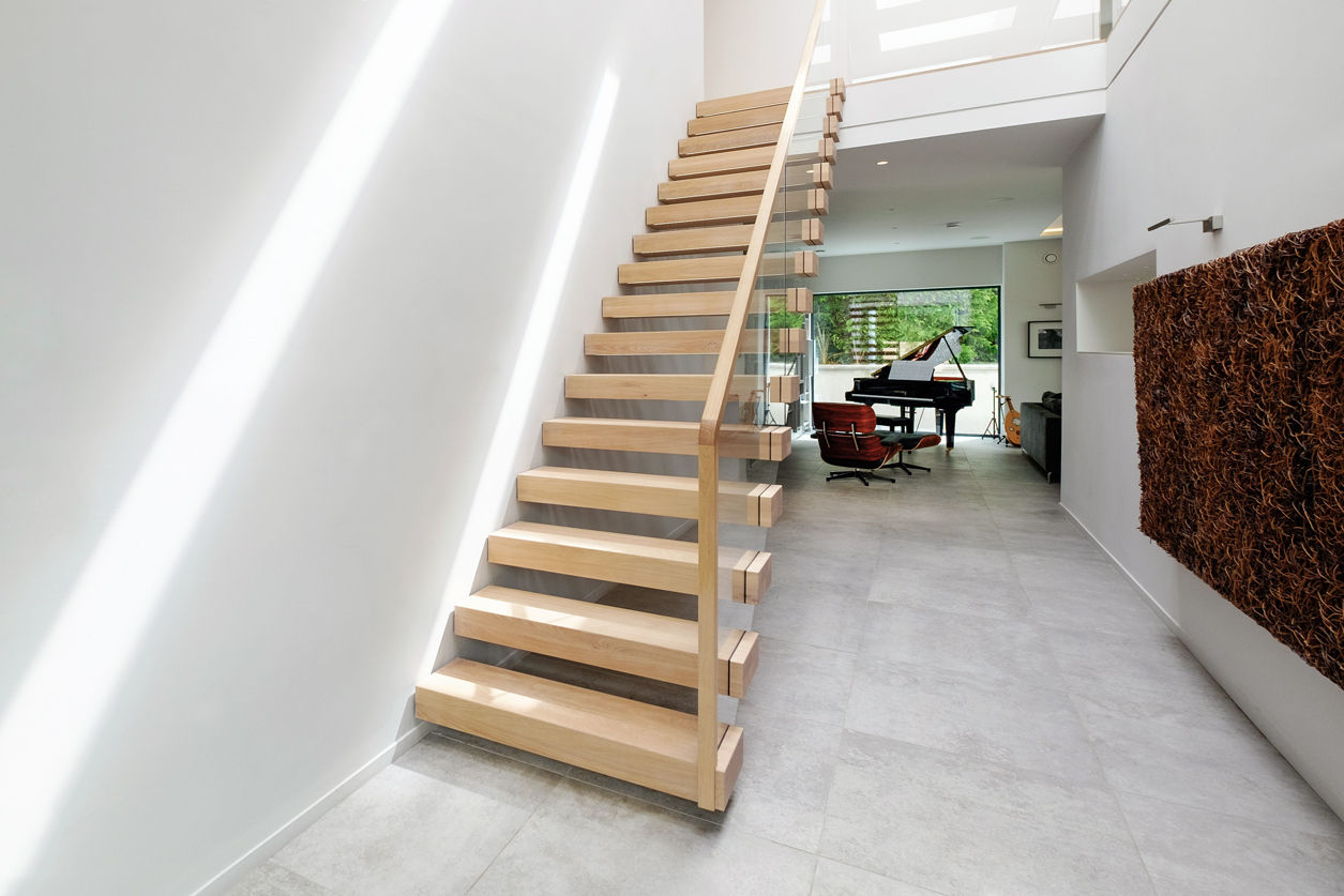 Cantilevered feature staircase with oak treads and glass balustrade. Baby grand piano and Eames Lounge Chair. Large sculpture on wall.