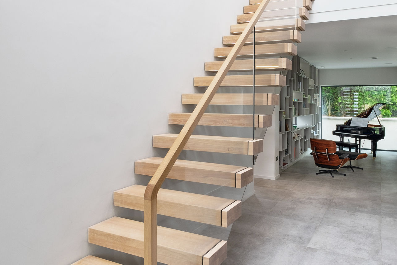 Cantilevered floating feature staircase with oak treads and glass balustrade. Baby grand piano and Eames Lounge Chair in background.