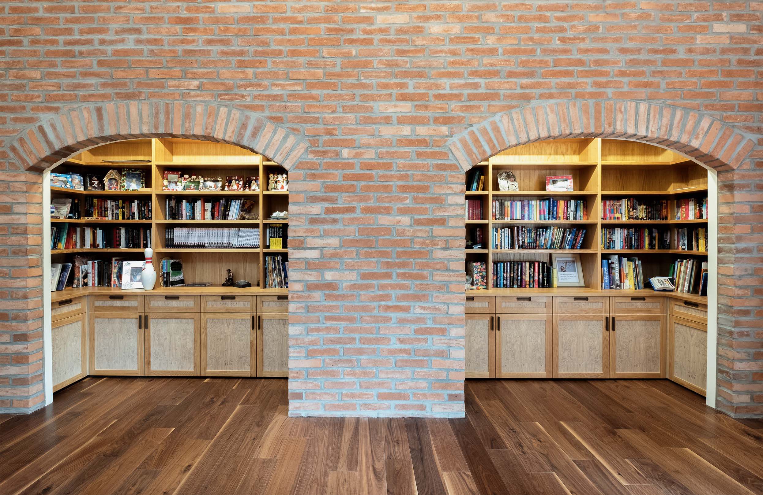 Oak bookcases and cabinets with pippy oak veneered doors set within two brick archways. Bookcases filled with books and ornaments.