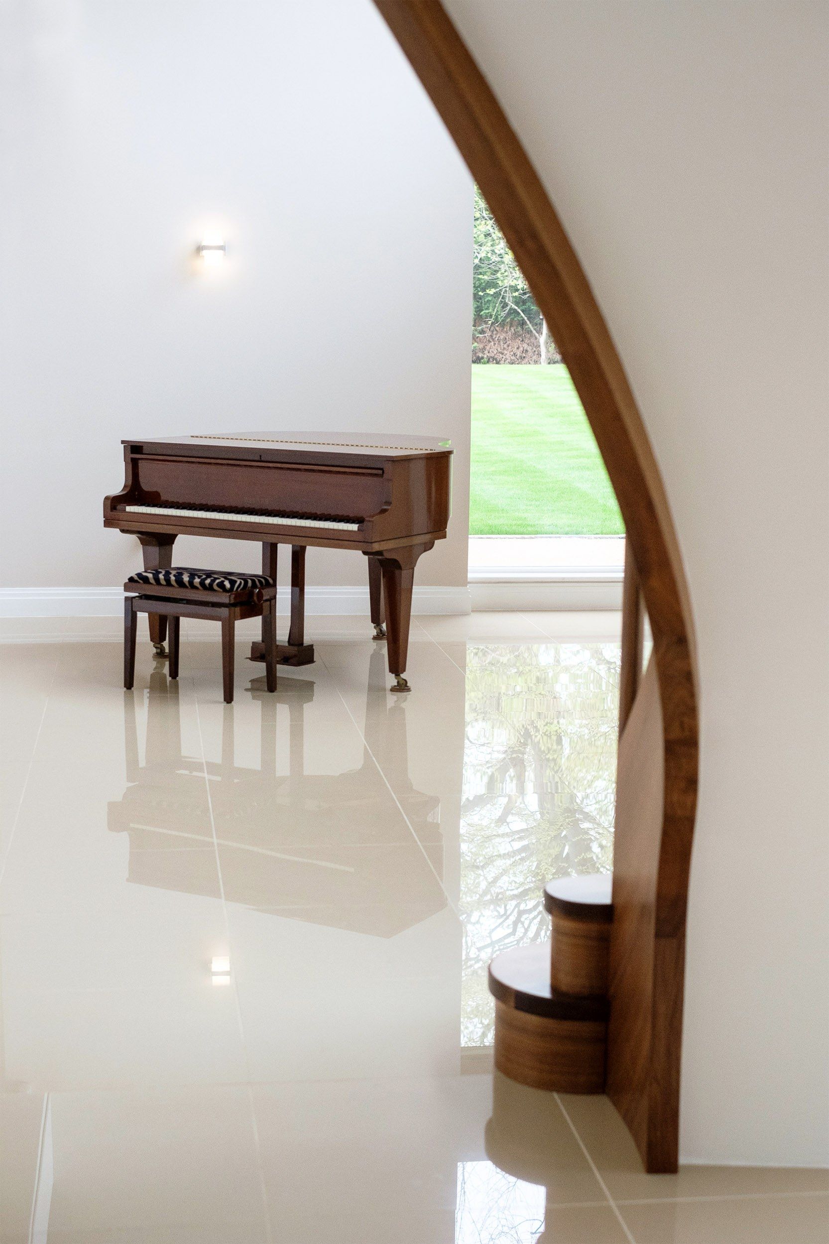 Side view of sweeping curved walnut staircase with baby grand piano.