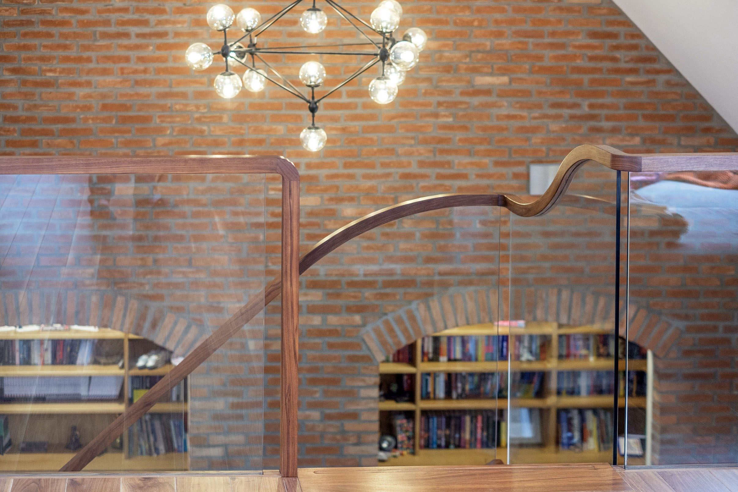 Sweeping curved glass balustrade against brick wall with fitted oak cabinets.