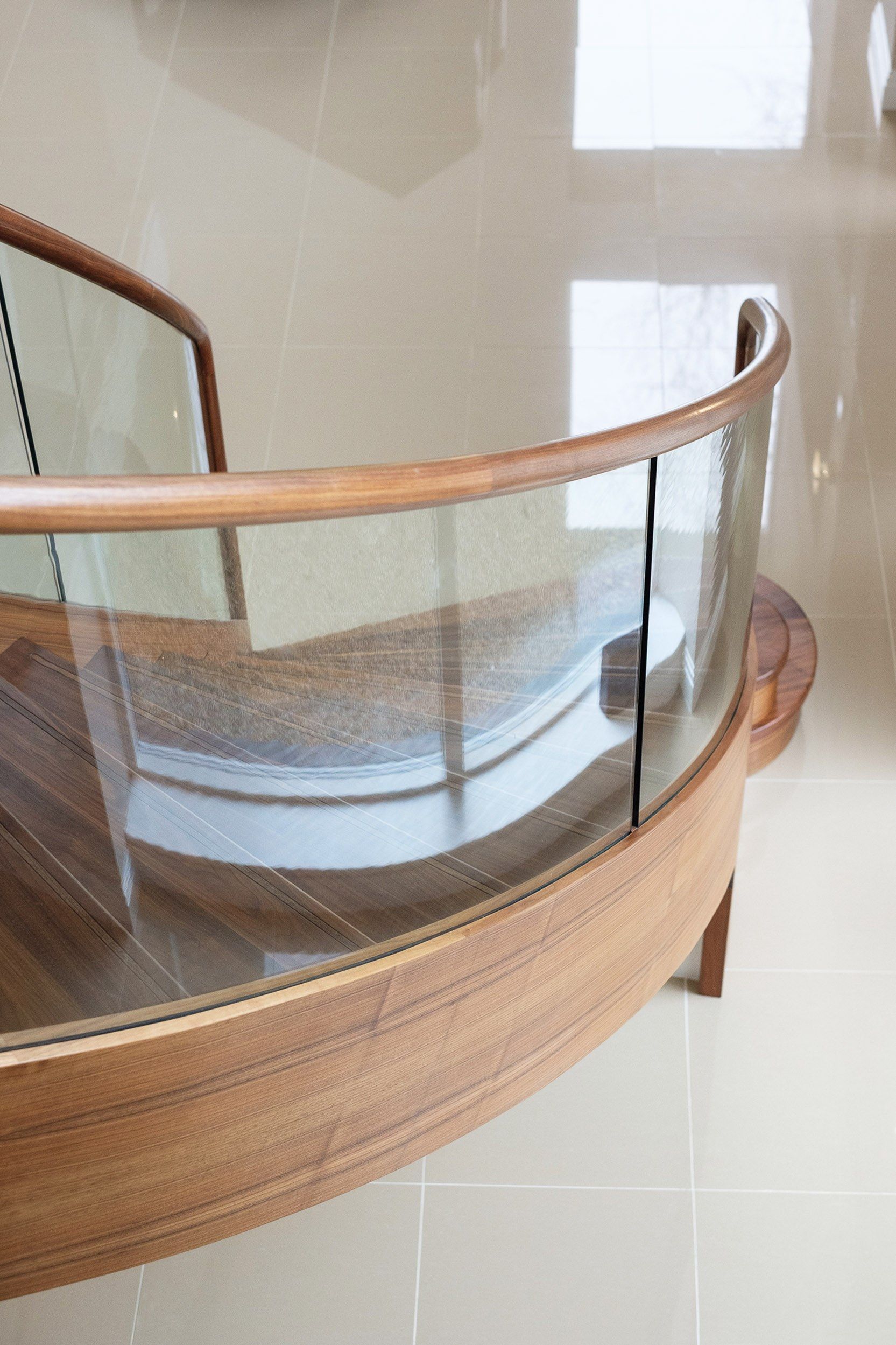 Plan view of sweeping curved walnut stair with curved glass and polished grey tile floor.