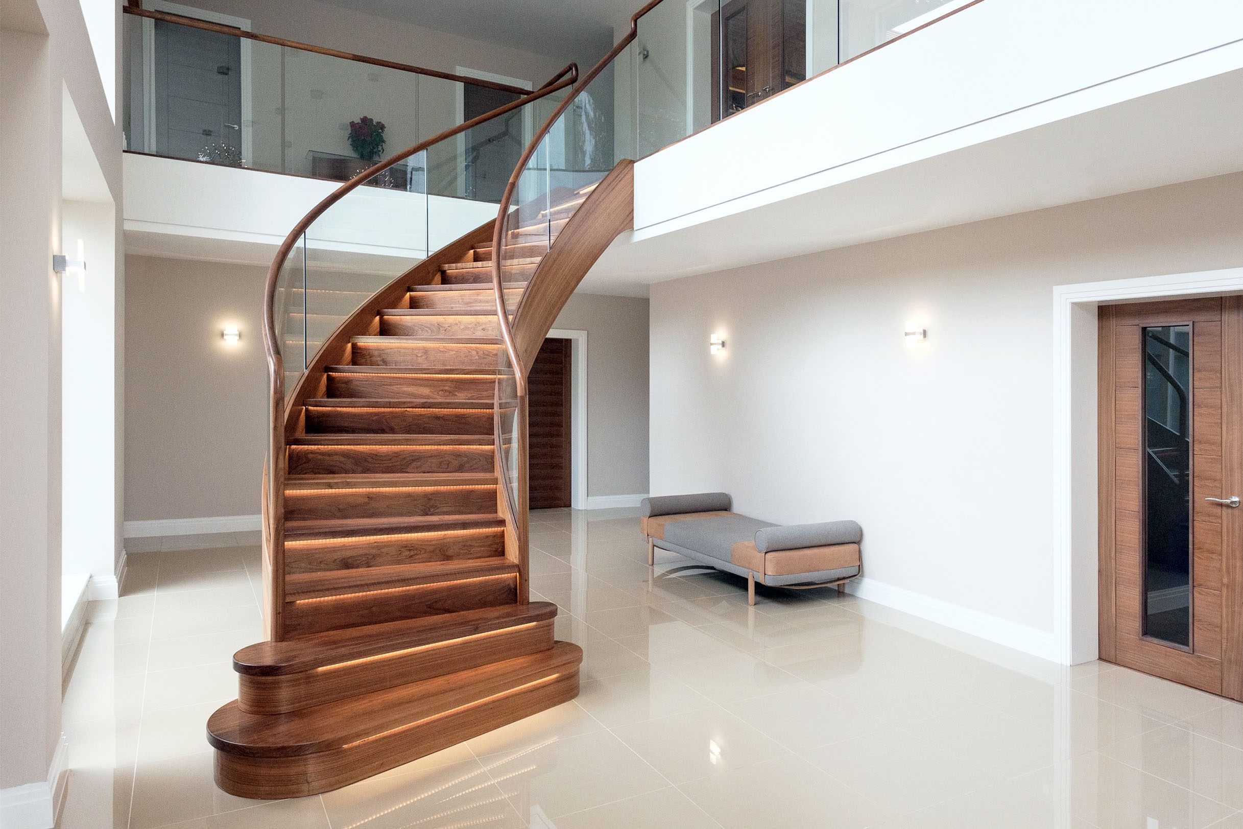 Interior view of sweeping curved walnut stair with curved glass and tread lighting.