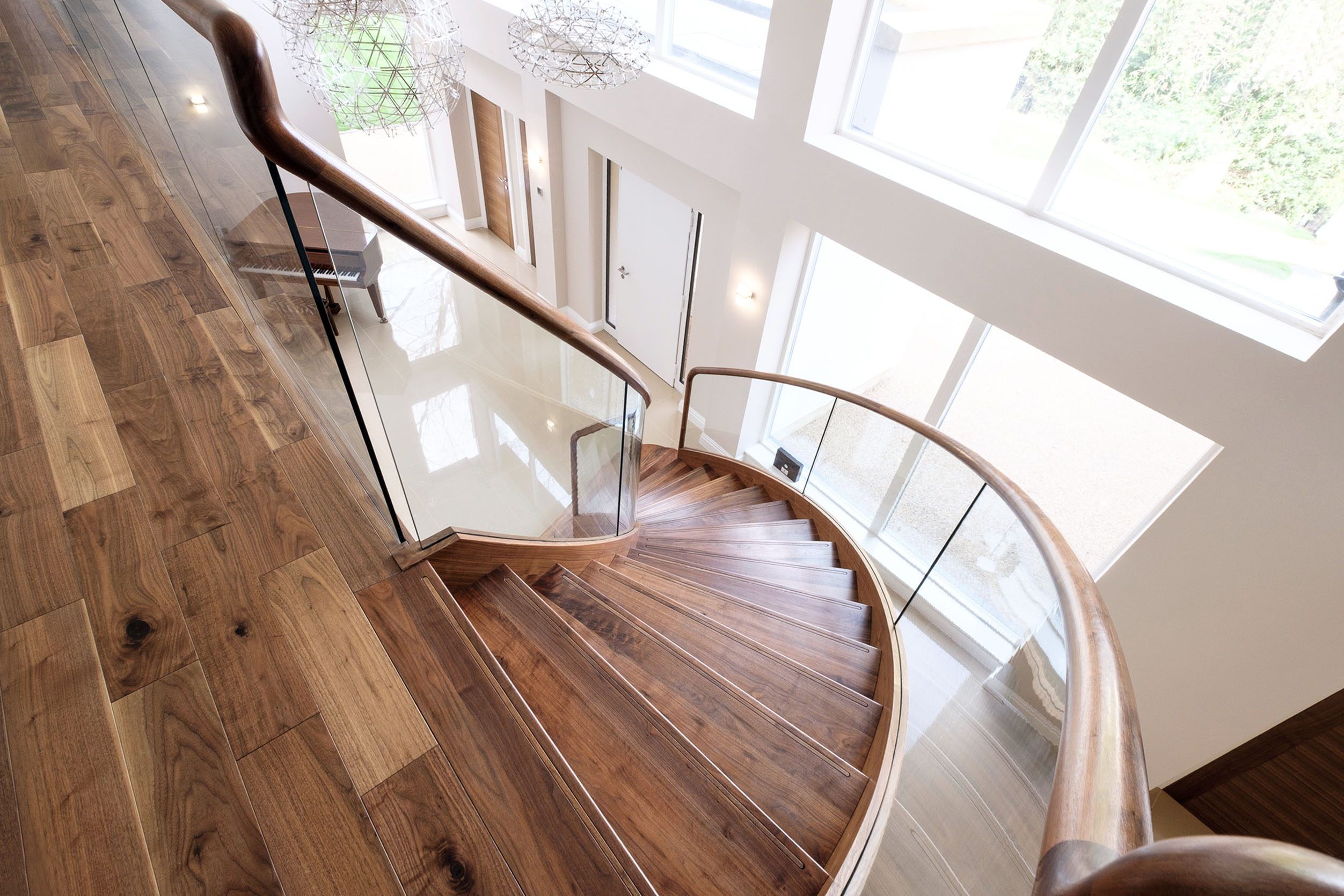 Sweeping curved walnut stair with curved glass and tread lighting in large white home with baby grand piano.