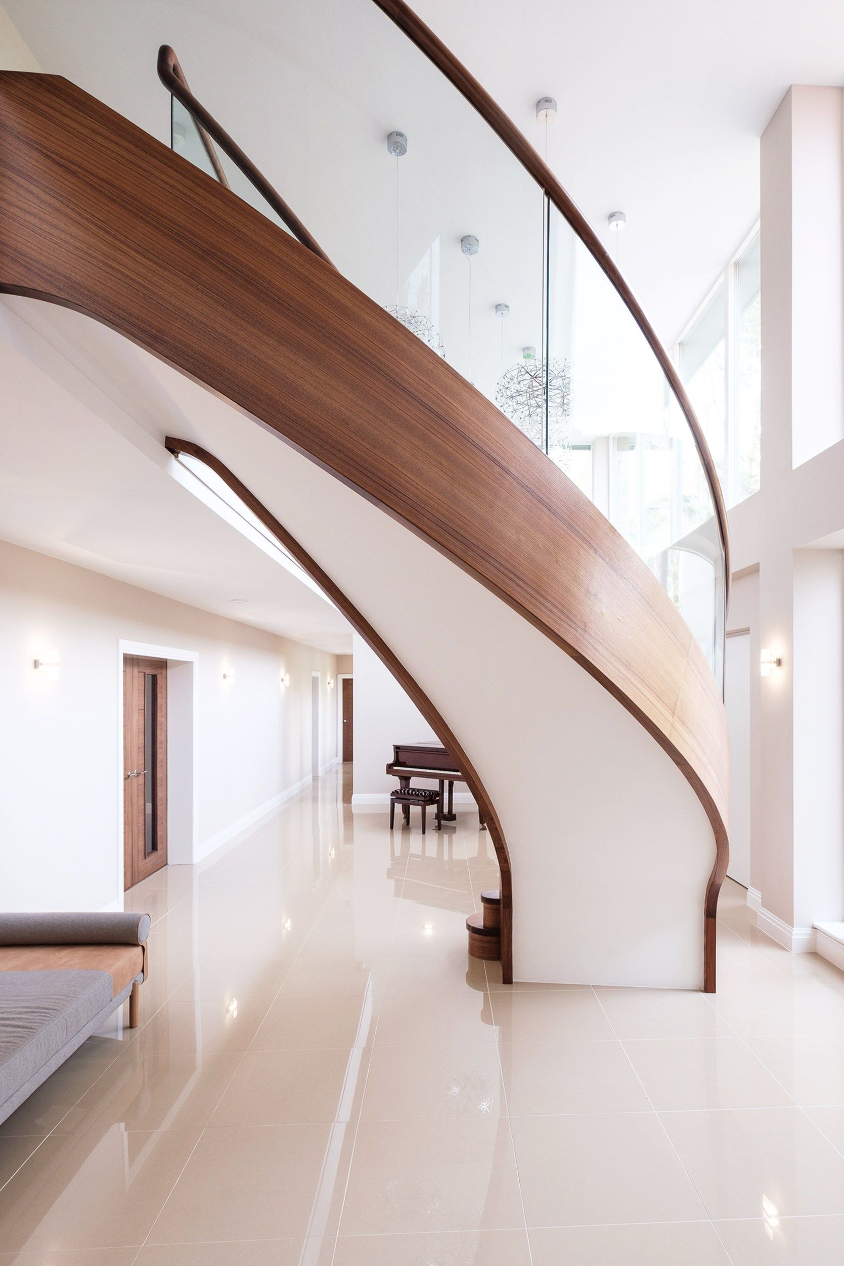 Underside of view of sweeping curved walnut stair with curved glass in large home with baby grand piano.