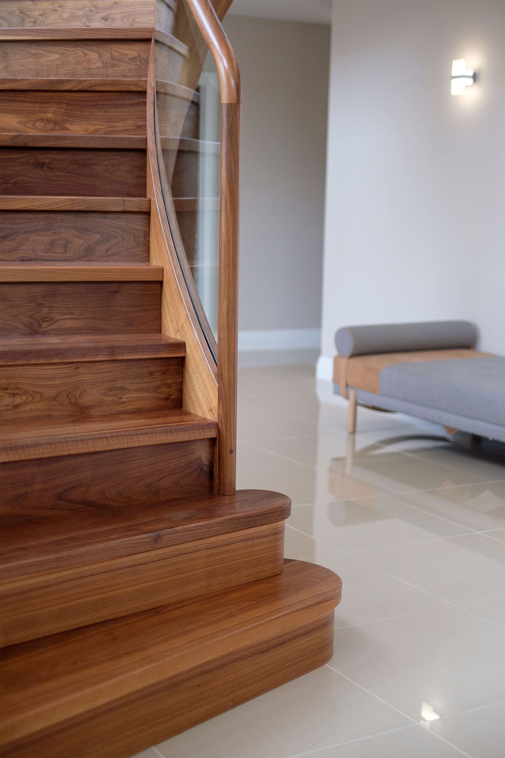 Walnut curved staircase with bullnose treads polished tile floor and modern bench.