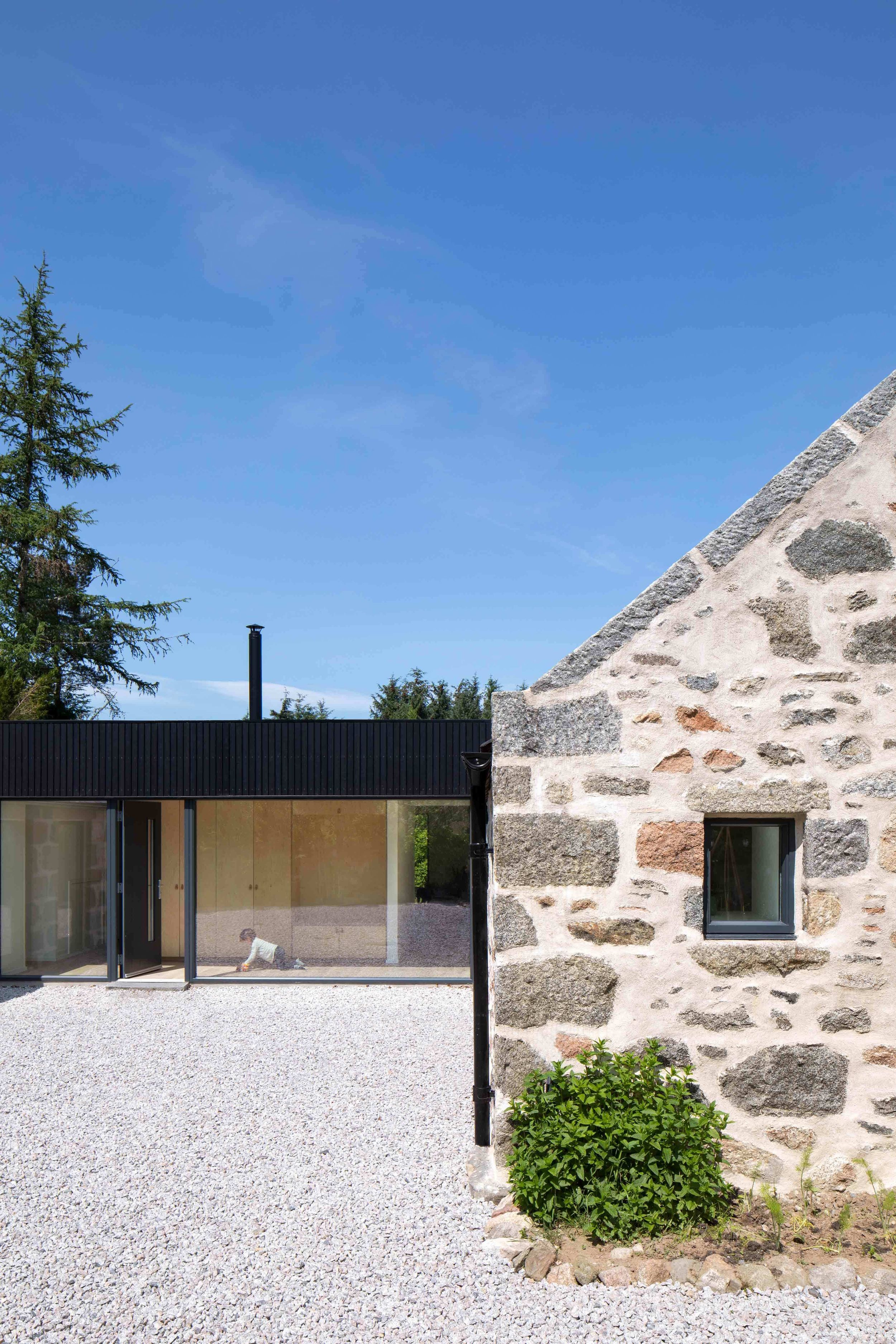 Traditional granite cottage with modern, blackened timber and glass extension with child crawling