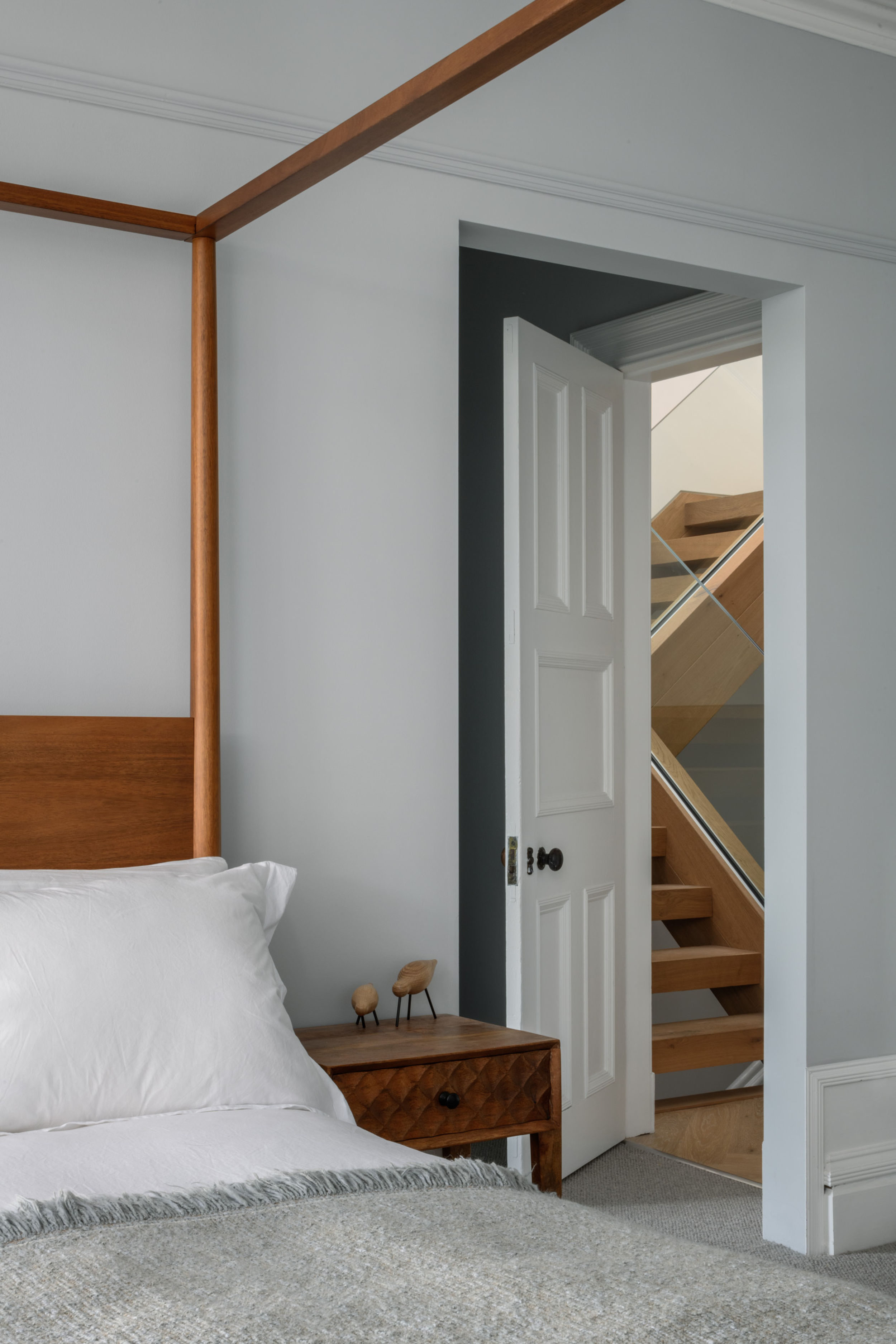 Bedroom with four poster bed, bedside table and white bedding. Doorway with view of staircase.