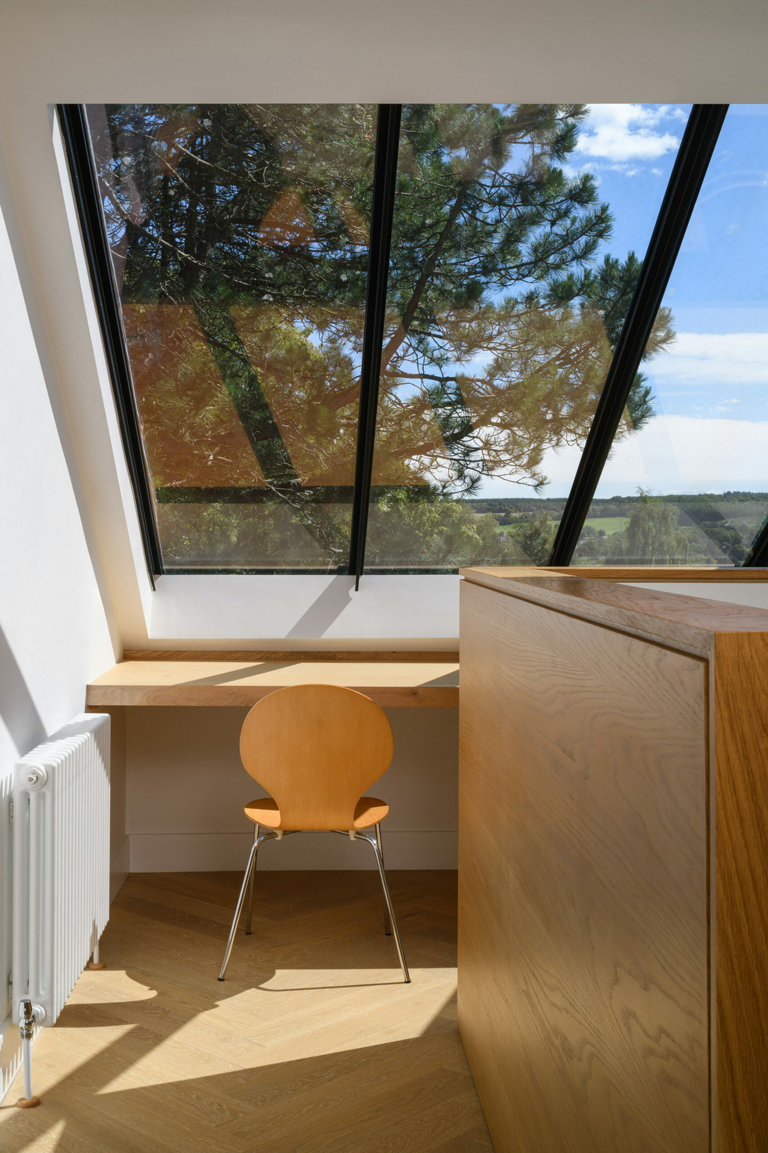 Desk space with single wooden chair in roofscape with large glazing