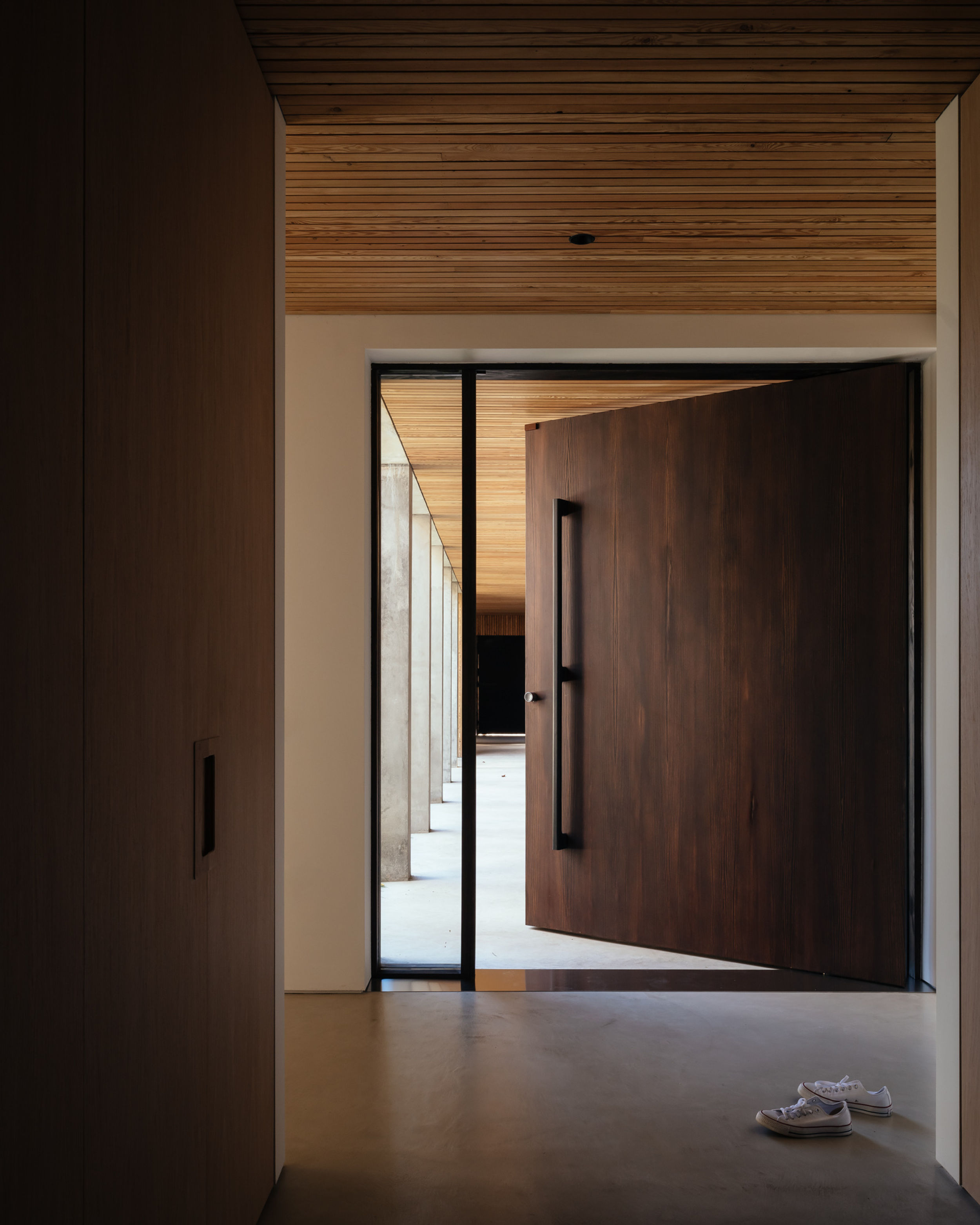 A smoked larch pivot front door is partially opened, revealing a concrete colonnade outside.