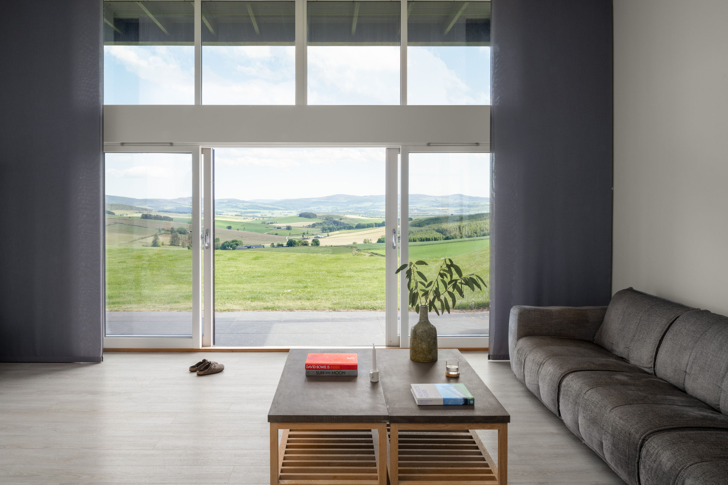 Long, grey couch with colourful books on a coffee table. Expansive views of landscape.