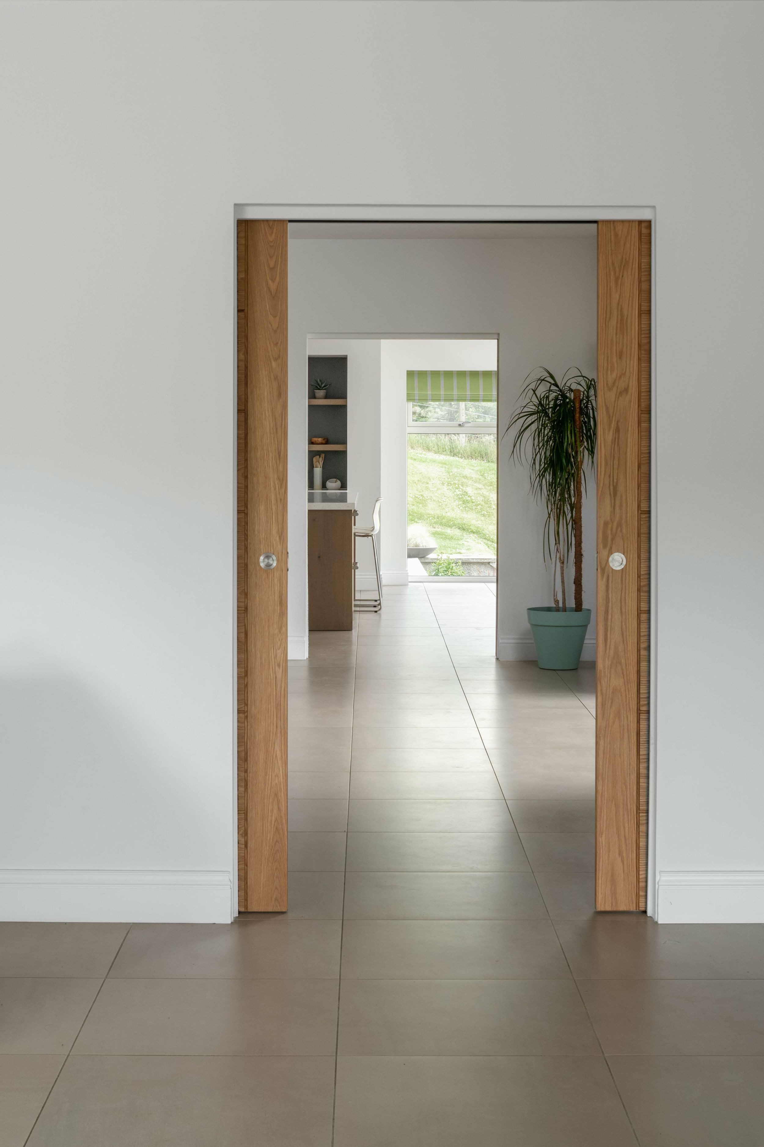 Looking though a timber sliding door into a kitchen. Large, beige tile floor tiles.